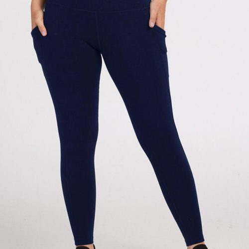 A person wearing the Piper Pocket Petite leggings in deep navy from Woolx, paired with black sneakers, stands against a plain white background. These high-waisted petite thermal leggings blend comfort and style effortlessly as the person casually places their hands in the spacious pockets.