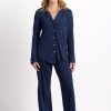 A person stands smiling, wearing the Harper FeatherTouch® Pajama Set - Starry Night by Woolx, a matching navy blue ensemble made of breathable Merino wool featuring a button-up top and long pants. The plain white background highlights the comfort and moisture-wicking qualities of their attire.